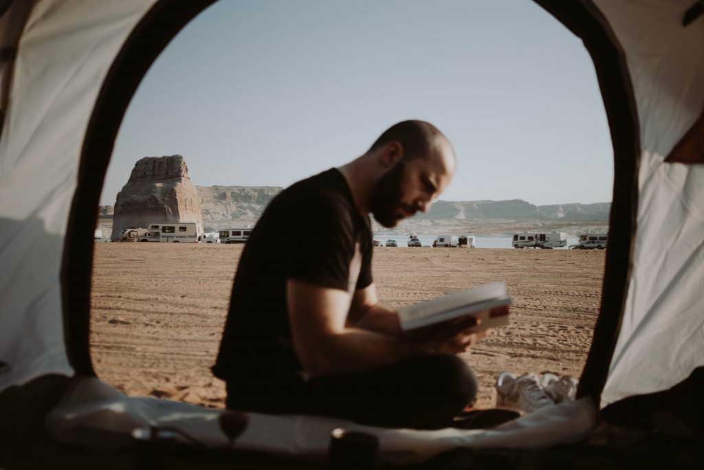 Homem lendo livros para aventureiros na barraca de camping