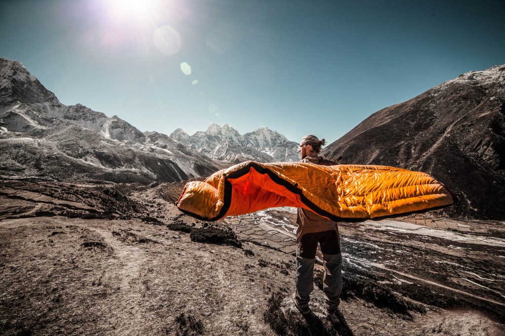Homem em meio às montanhas segura saco de dormir laranja