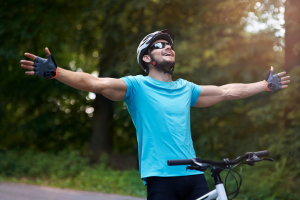 Homem usando luvas para ciclismo sobre uma bicicleta de braços abertos sorrindo