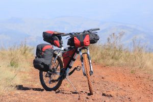 Bicicleta de cicloturismo em primeiro plano com carga em solo de terra