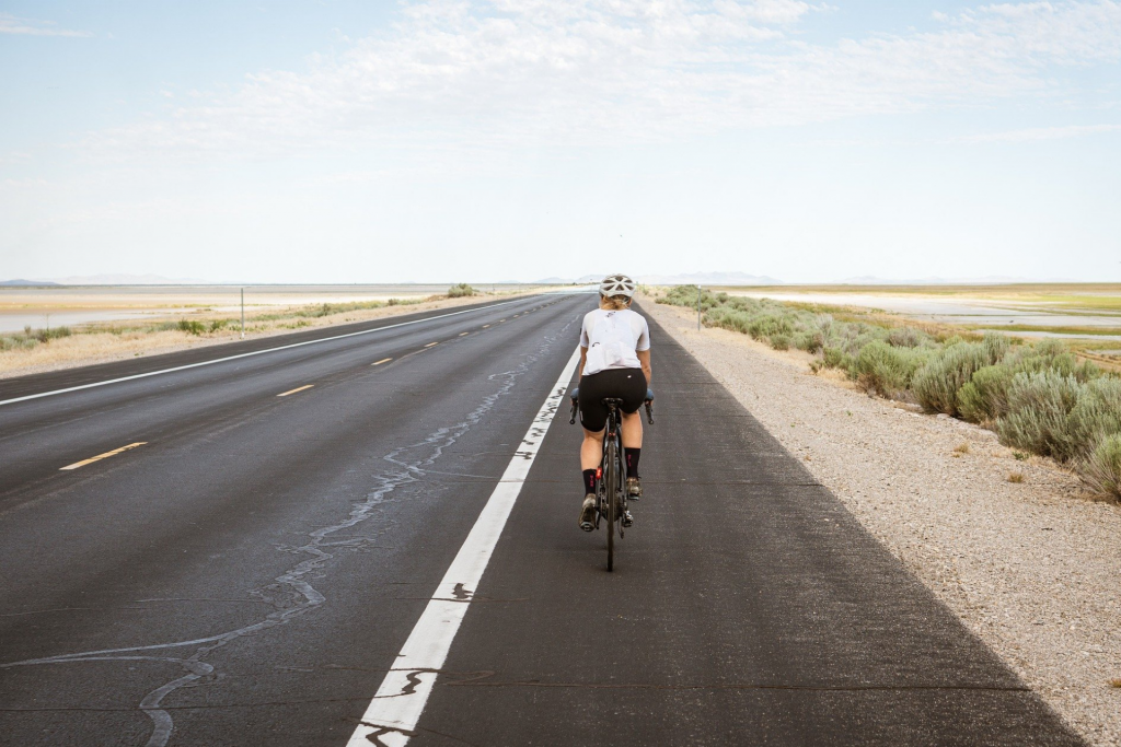 Ciclista fotografado de costas pedalando em uma rodovia vazia